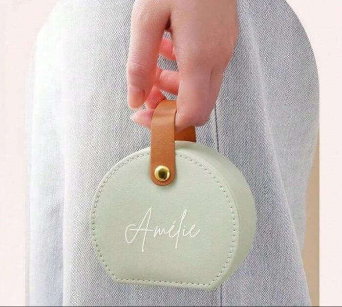 Boîte à bijoux personnalisée avec prénom "Amélie" en forme de sac à main tenue par une main féminine, idéale comme cadeau pour femmes.