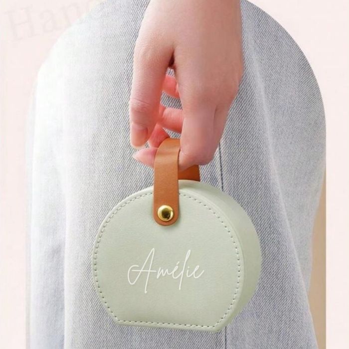 Boîte à bijoux personnalisée avec prénom "Amélie" en forme de sac à main tenue par une main féminine, idéale comme cadeau pour femmes.