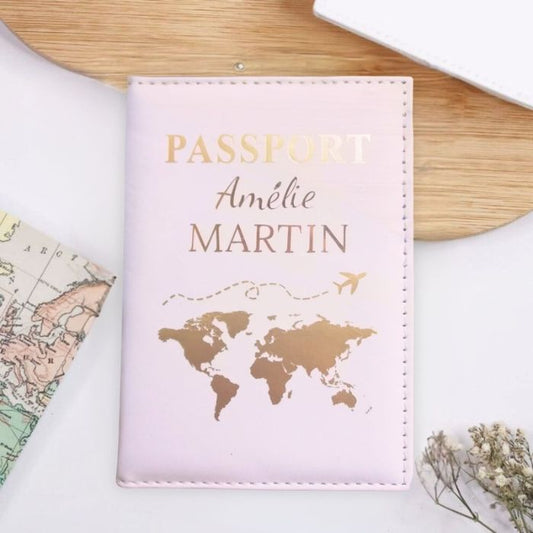 Protège-passeport personnalisé de couleur rose pâle avec le nom Amélie Martin gravé en lettres dorées élégantes. L'étui présente un motif de carte du monde dorée avec un avion en vol. Accessoire chic et pratique pour voyager avec style.